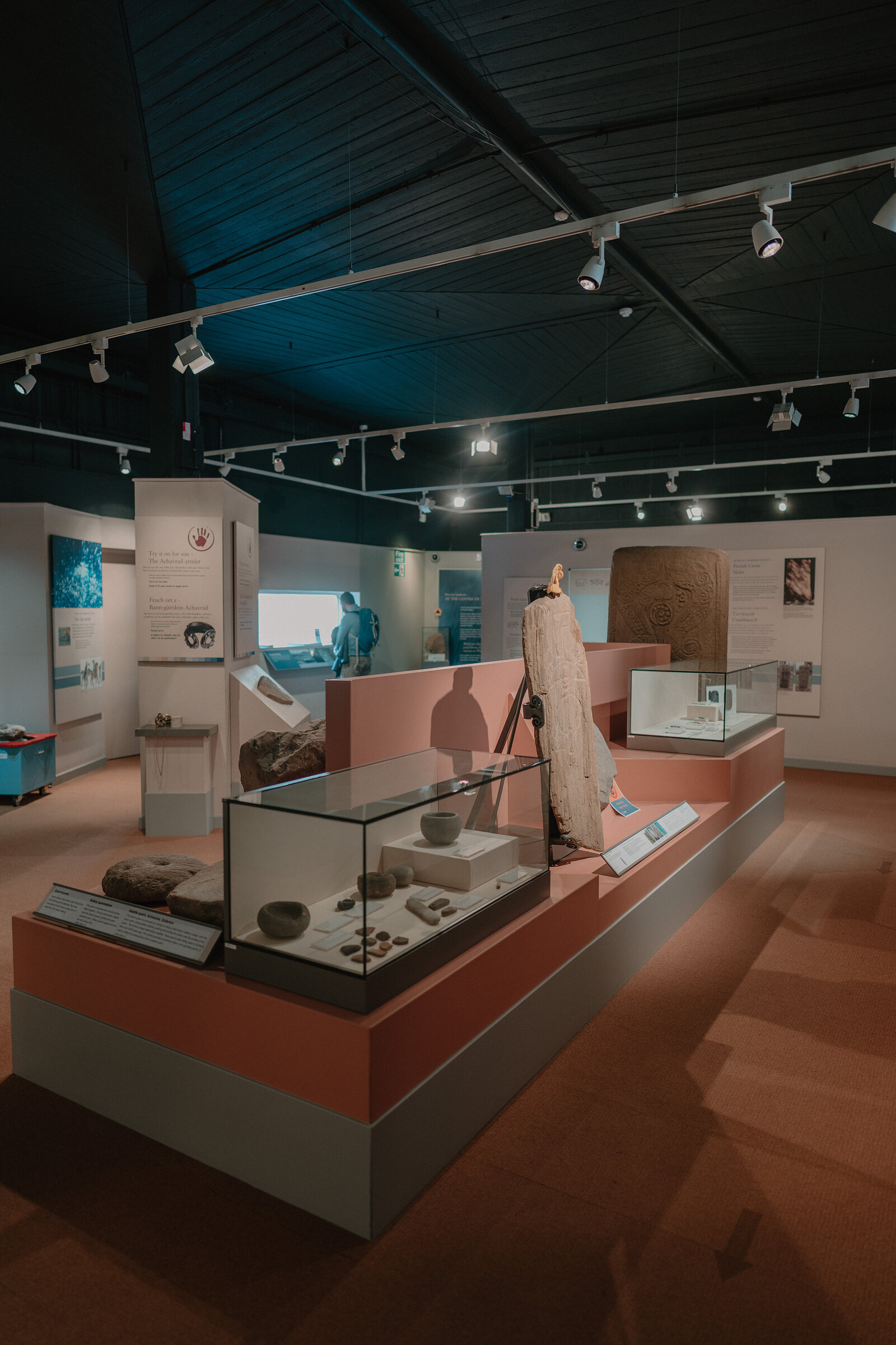 A museum display shows a carved stone cross slab and archaeological finds in glass cases, information panels lining the raised platform.