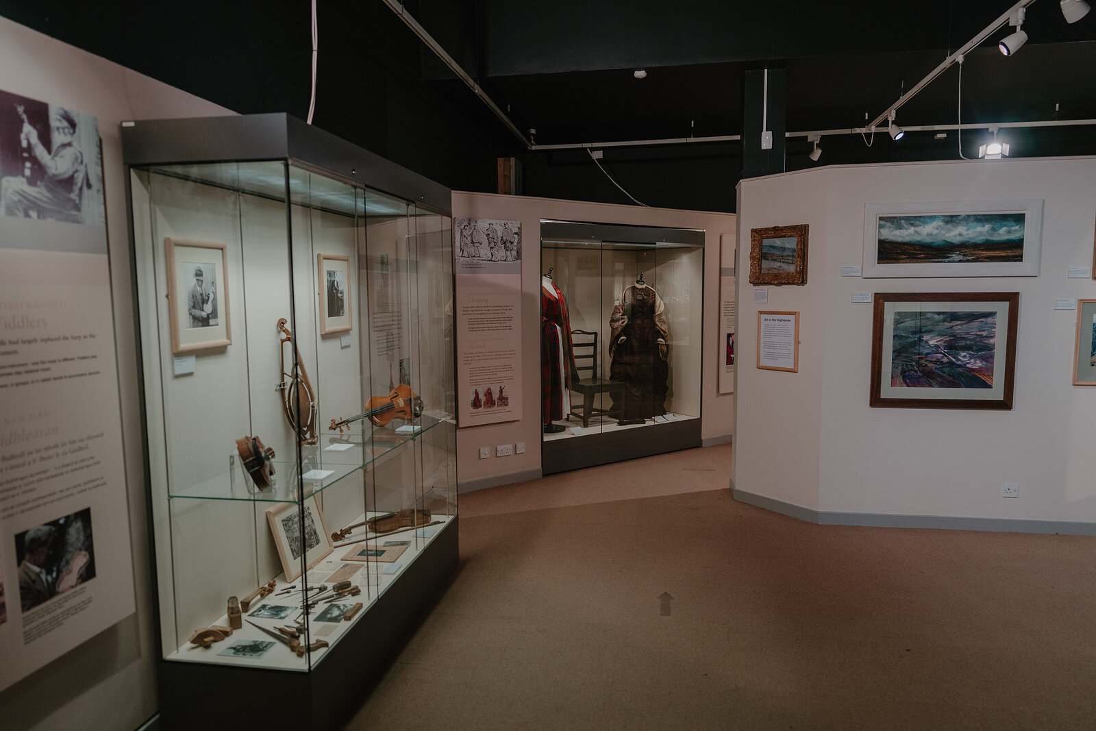 A museum gallery displays fishing tools, a diver's helmet and framed paintings of stormy seas in glass cases along curved walls.