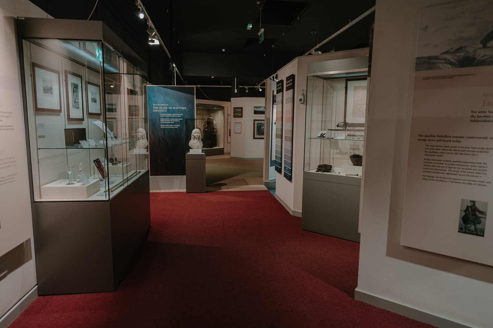 A museum gallery displays a marble bust beside a panel reading 'The Home of Scottish Identity', a framed portrait and glass cases lining the dark walls.