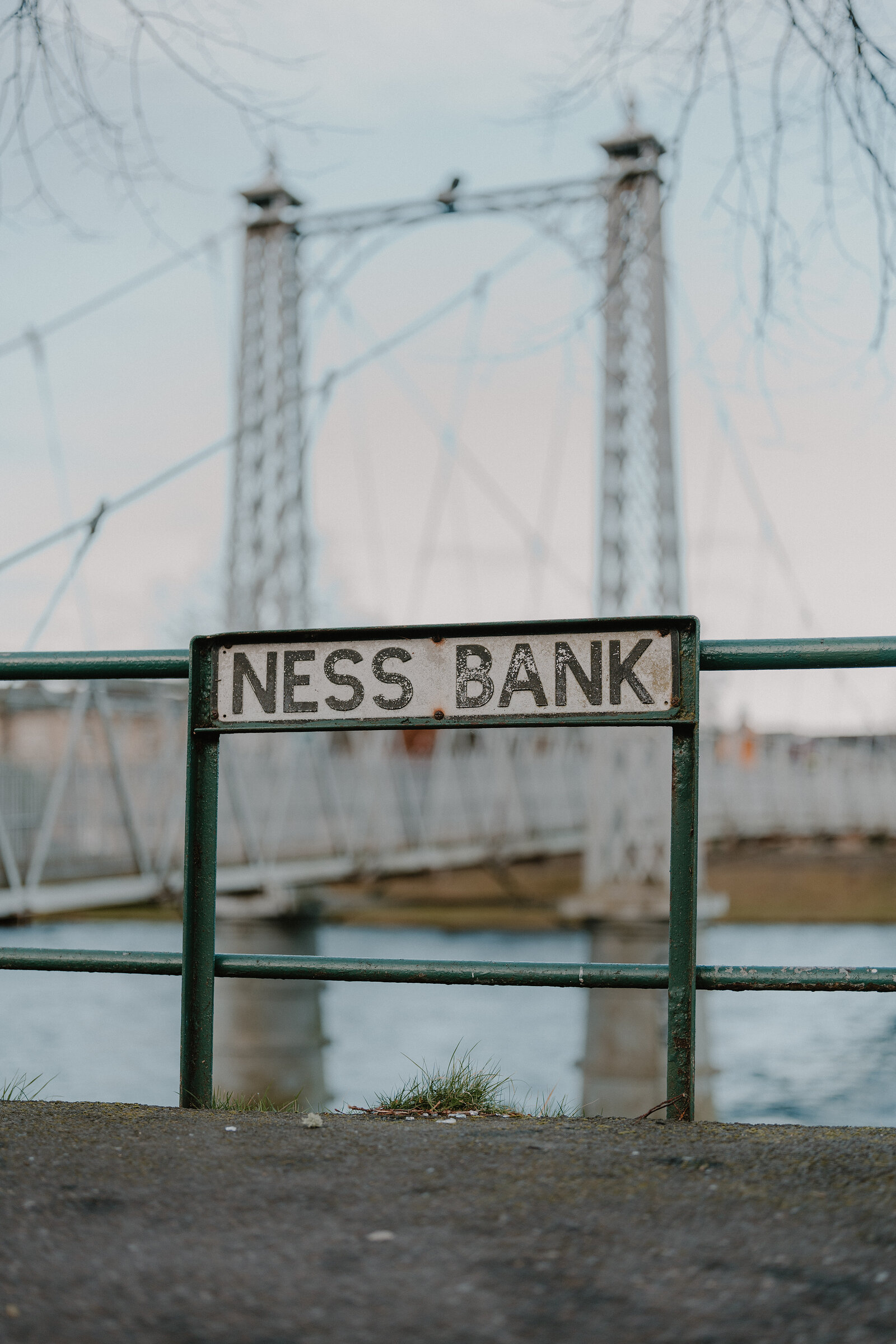 A metal plaque reading 'W. Smith & Son, Ness Ironworks, Inverness' is fixed to a lattice tower on a white suspension footbridge.