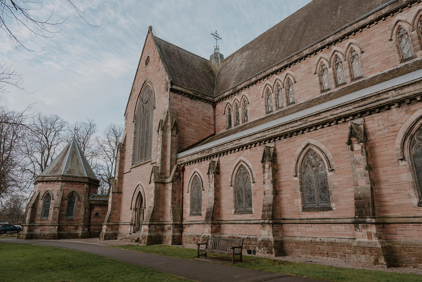 A row of tall lancet windows with stone tracery lines the side of a sandstone church, a small octagonal turret and porch standing beside it.