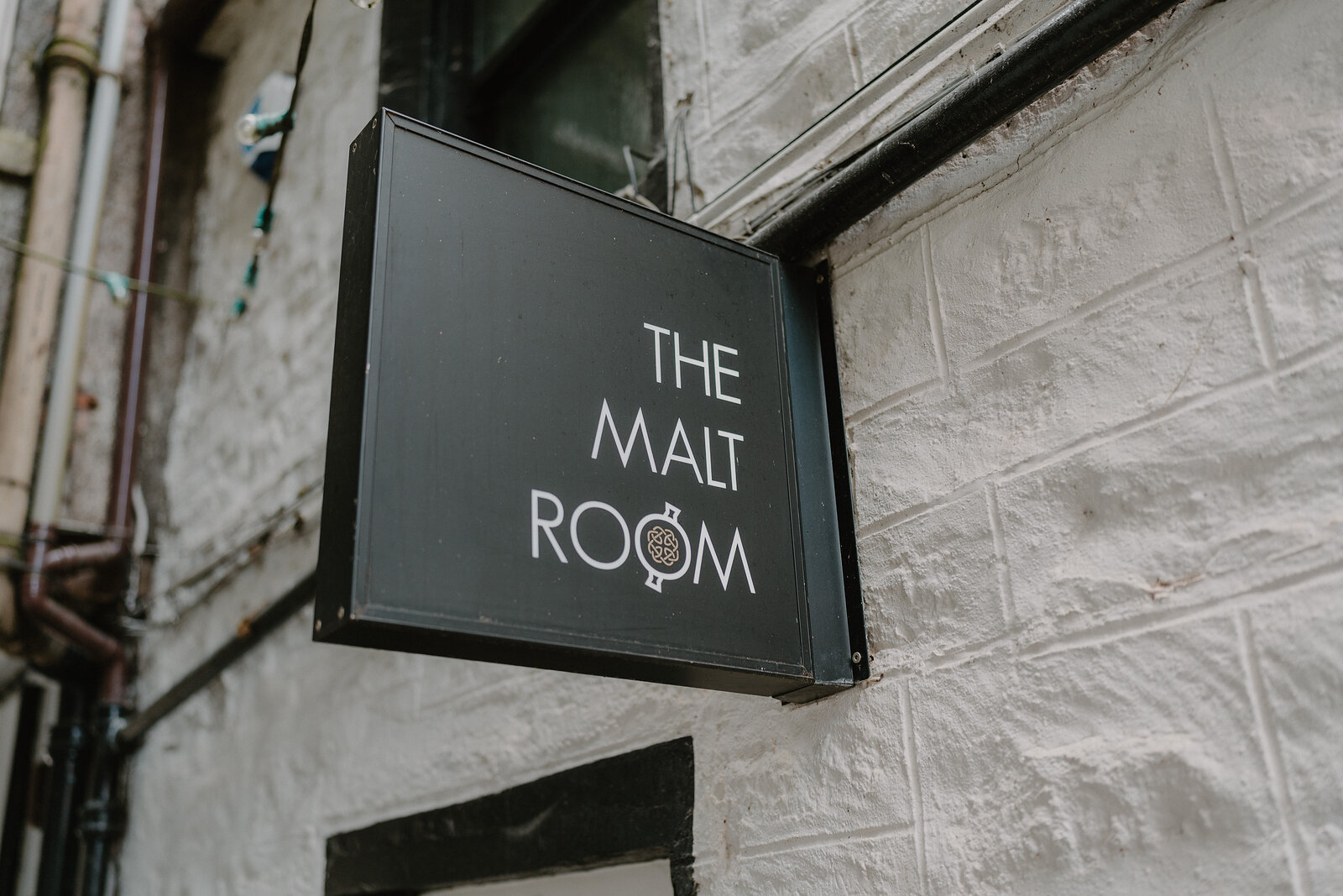 A projecting sign reading "The Malt Room" hangs from a stone wall above a doorway.