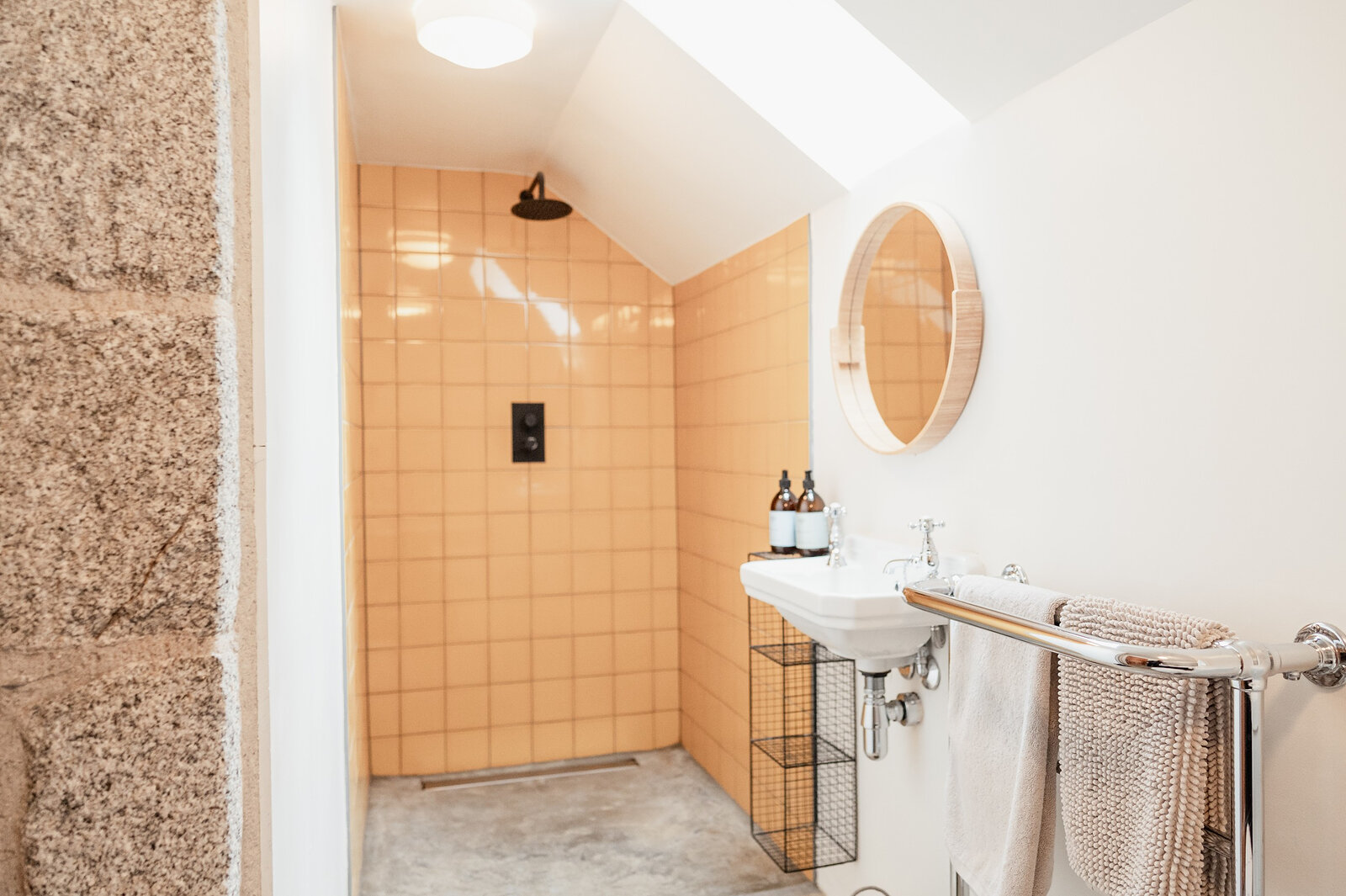 The big walk-in shower, tiled in apricot under a sloping ceiling, with a round mirror over the basin.