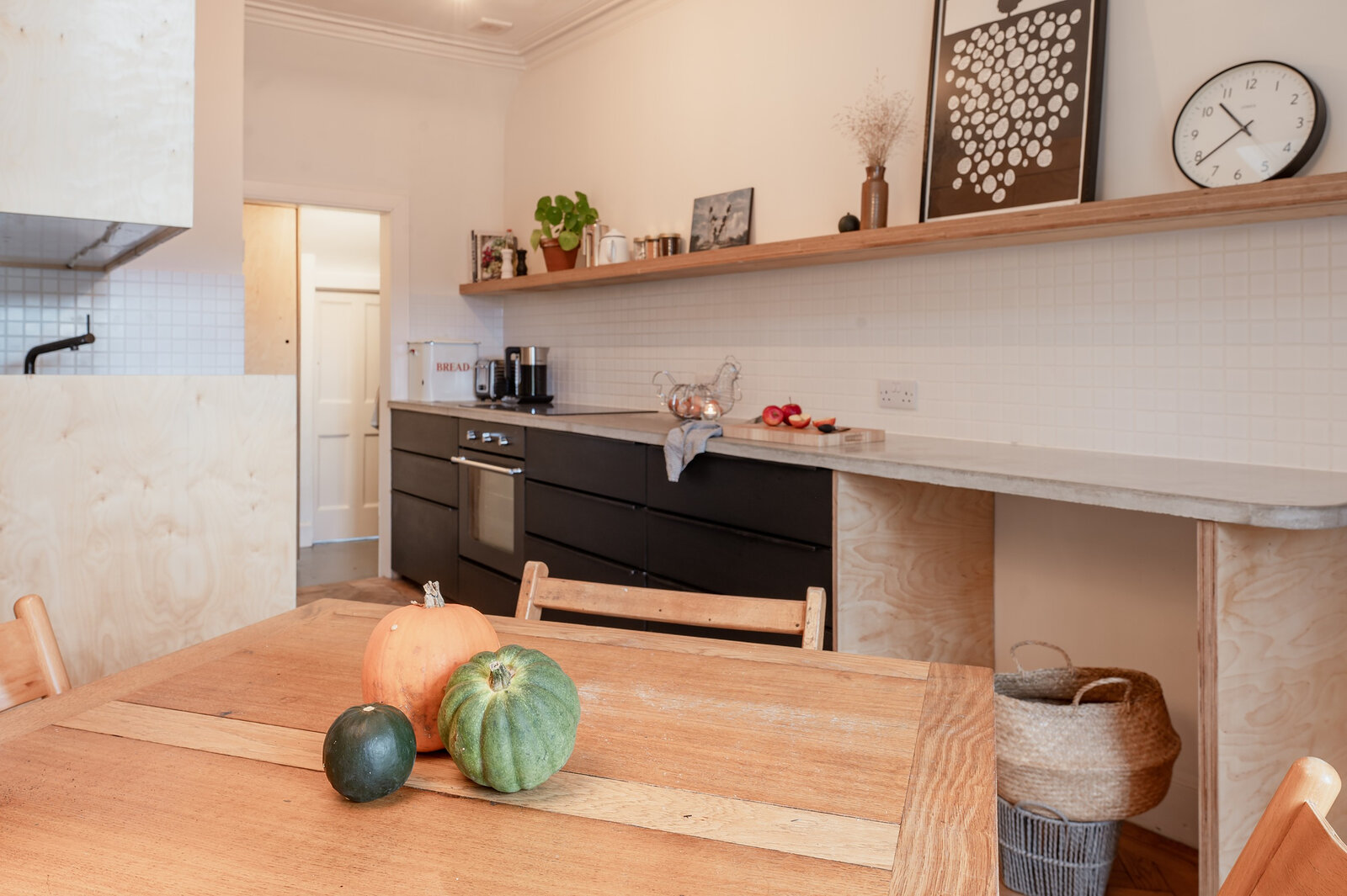 The kitchen and dining room, with a wooden table set with squashes, black units and a long shelf.