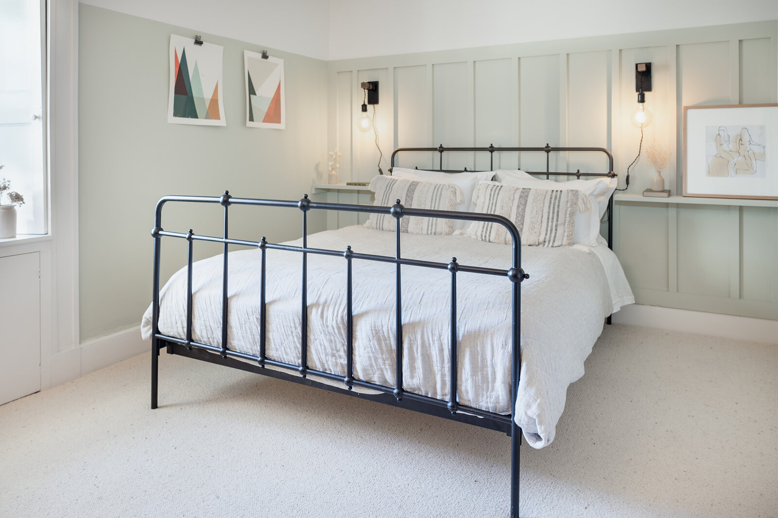 The king-size bedroom with a black iron bed, white linen and pale green panelled walls.