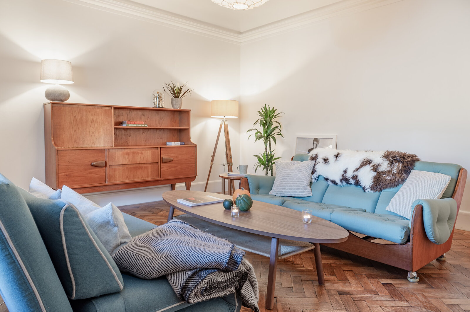The sitting room from the other end, with a teak sideboard, a standing lamp and a long oval coffee table.