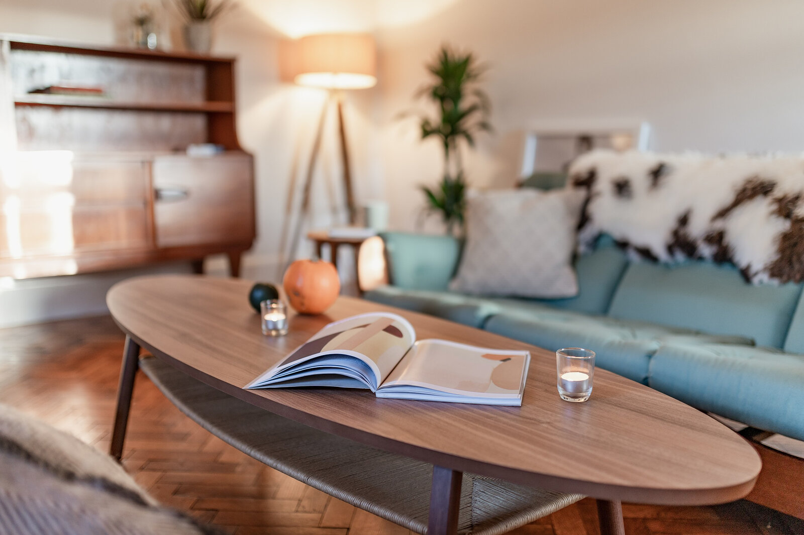 An open book and a pumpkin on the long oval coffee table, the sofa and sideboard behind.