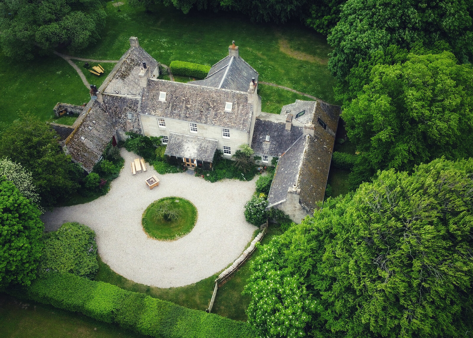 From above, the lodge and its stone outbuildings round a circle of gravel and lawn, with woodland all around.