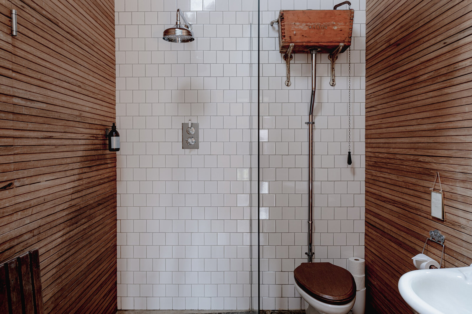 The timber-lined wet room with white tiles, a rainfall shower and an old-fashioned high cistern.