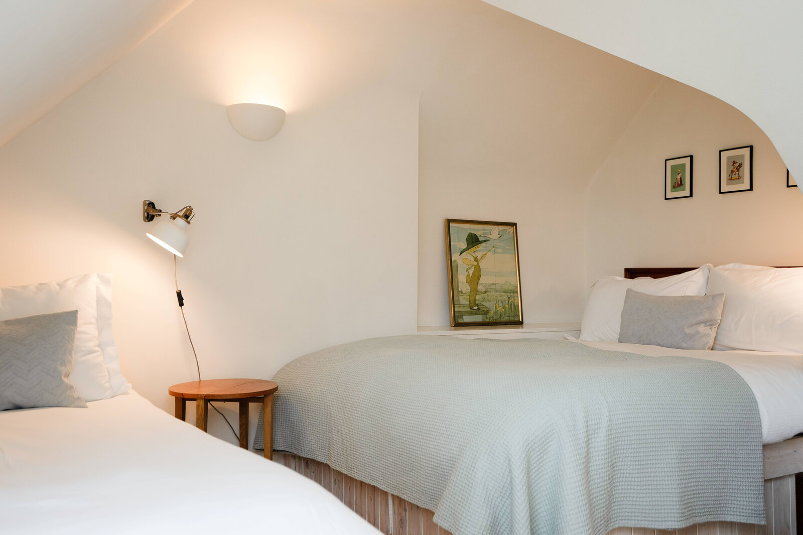 The upstairs bedroom under the eaves, with a double bed and a single, wall lamps and small framed prints.