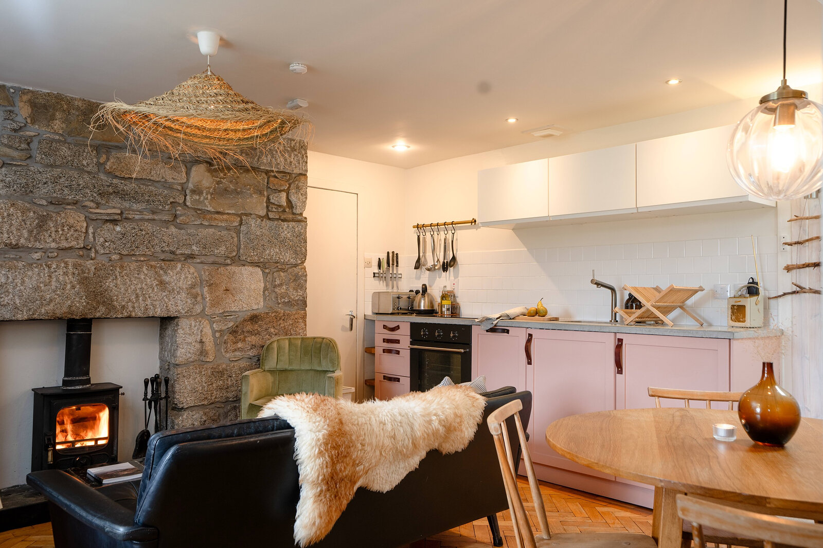 The kitchen and sitting room in one, with the stone fireplace and stove, pale pink units and a round table.