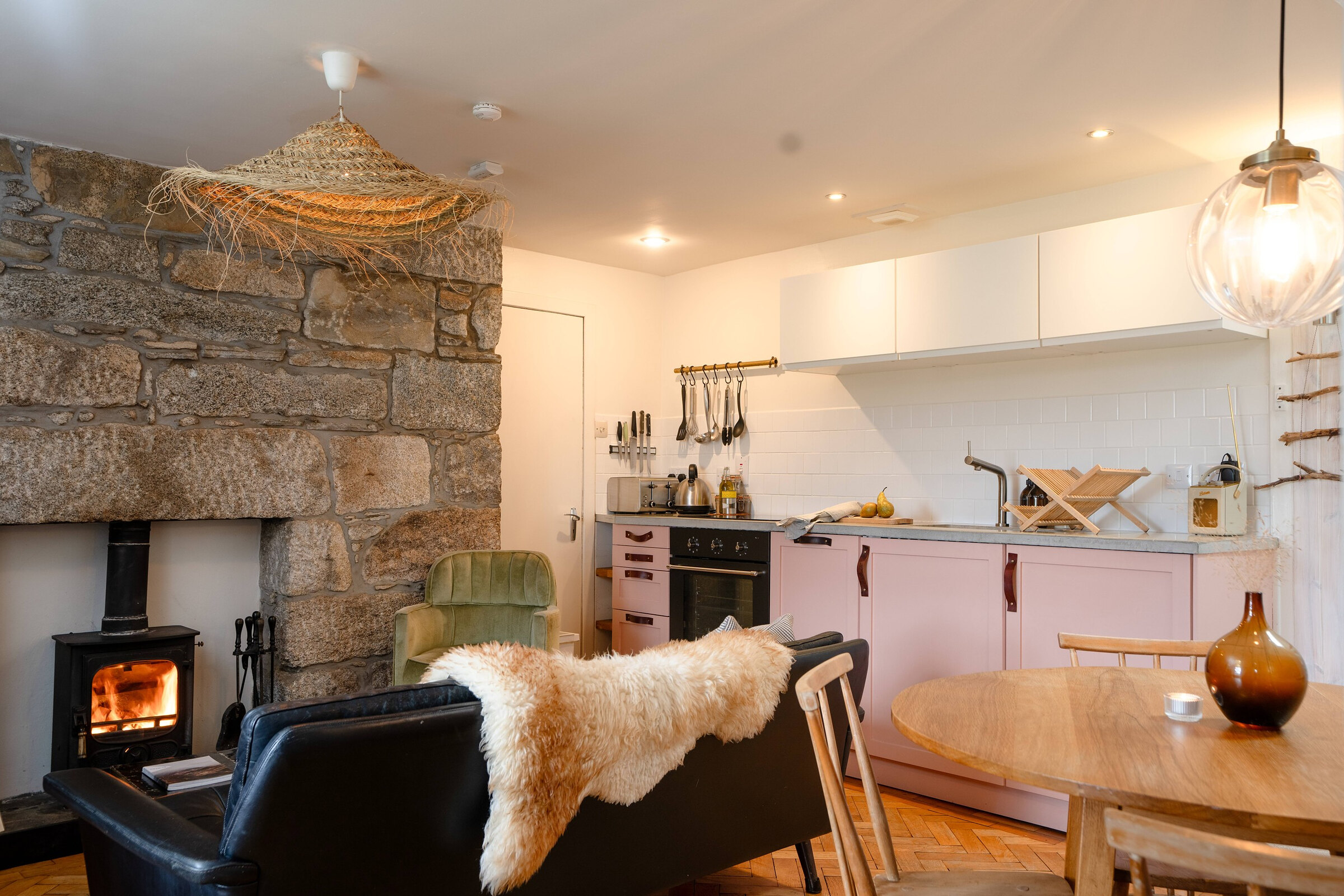 The kitchen and sitting room in one, with the stone fireplace and stove, pale pink units and a round table.