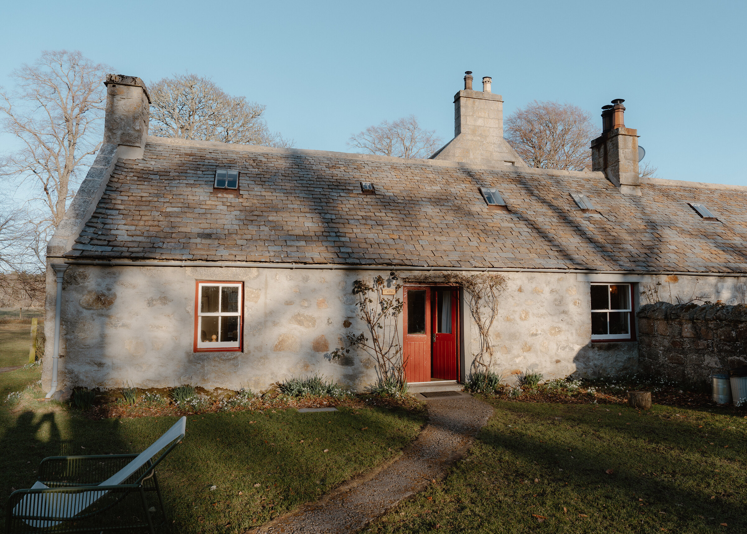 West Dell, a whitewashed stone cottage with a red door and a slate roof, in low winter sun.
