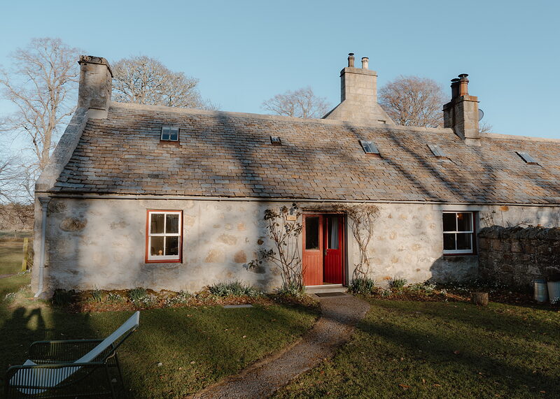 West Dell, a whitewashed stone cottage with a red door and a slate roof, in low winter sun.