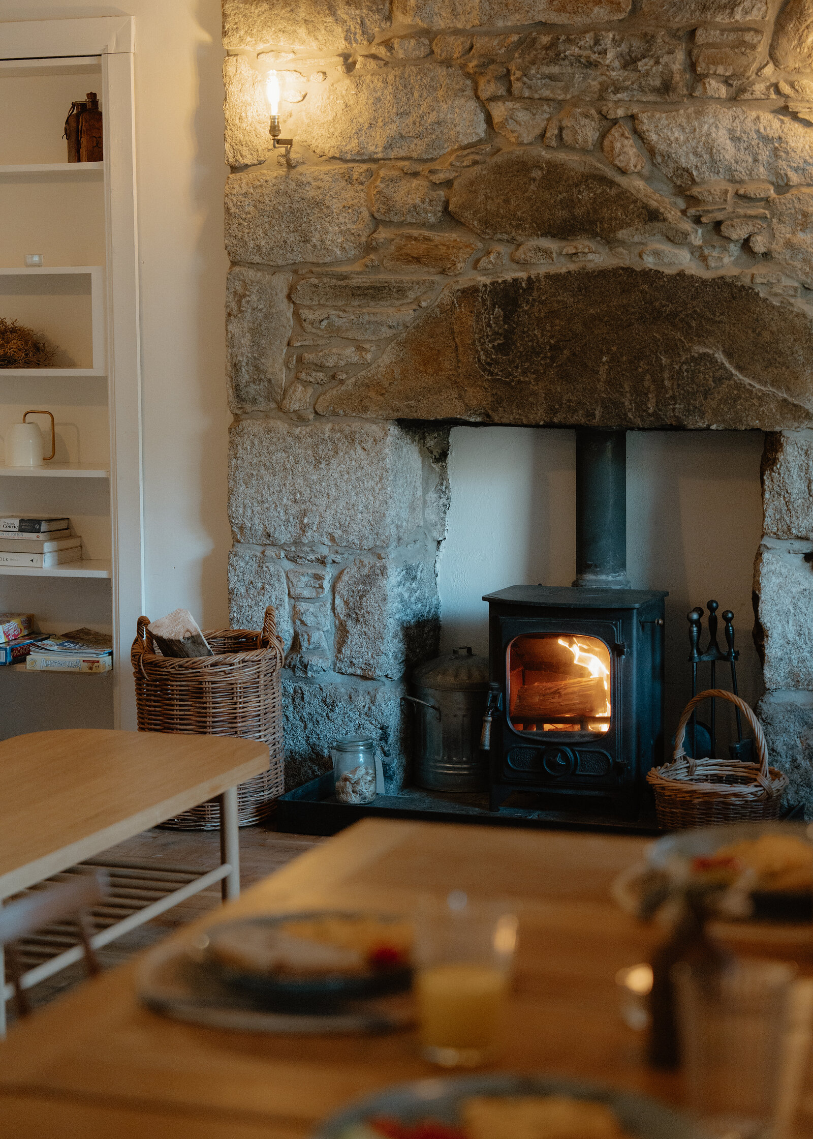 West Dell's wood-burning stove alight in its granite fireplace, a table laid for breakfast in front.