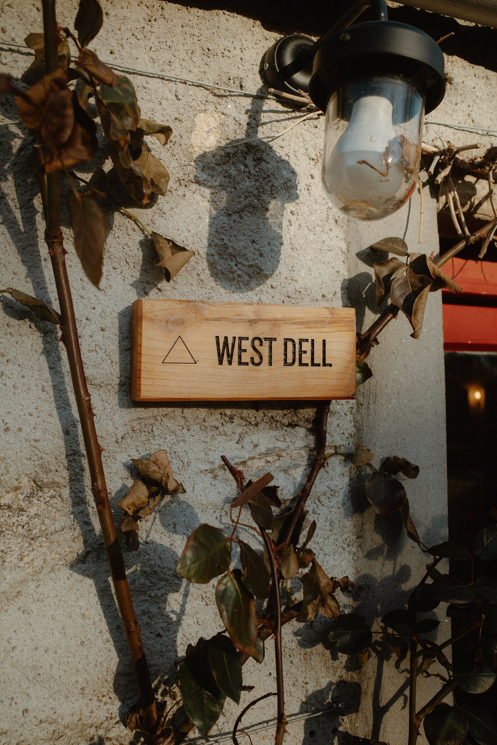 West Dell's wooden name sign on the whitewashed wall beside an outside lamp.
