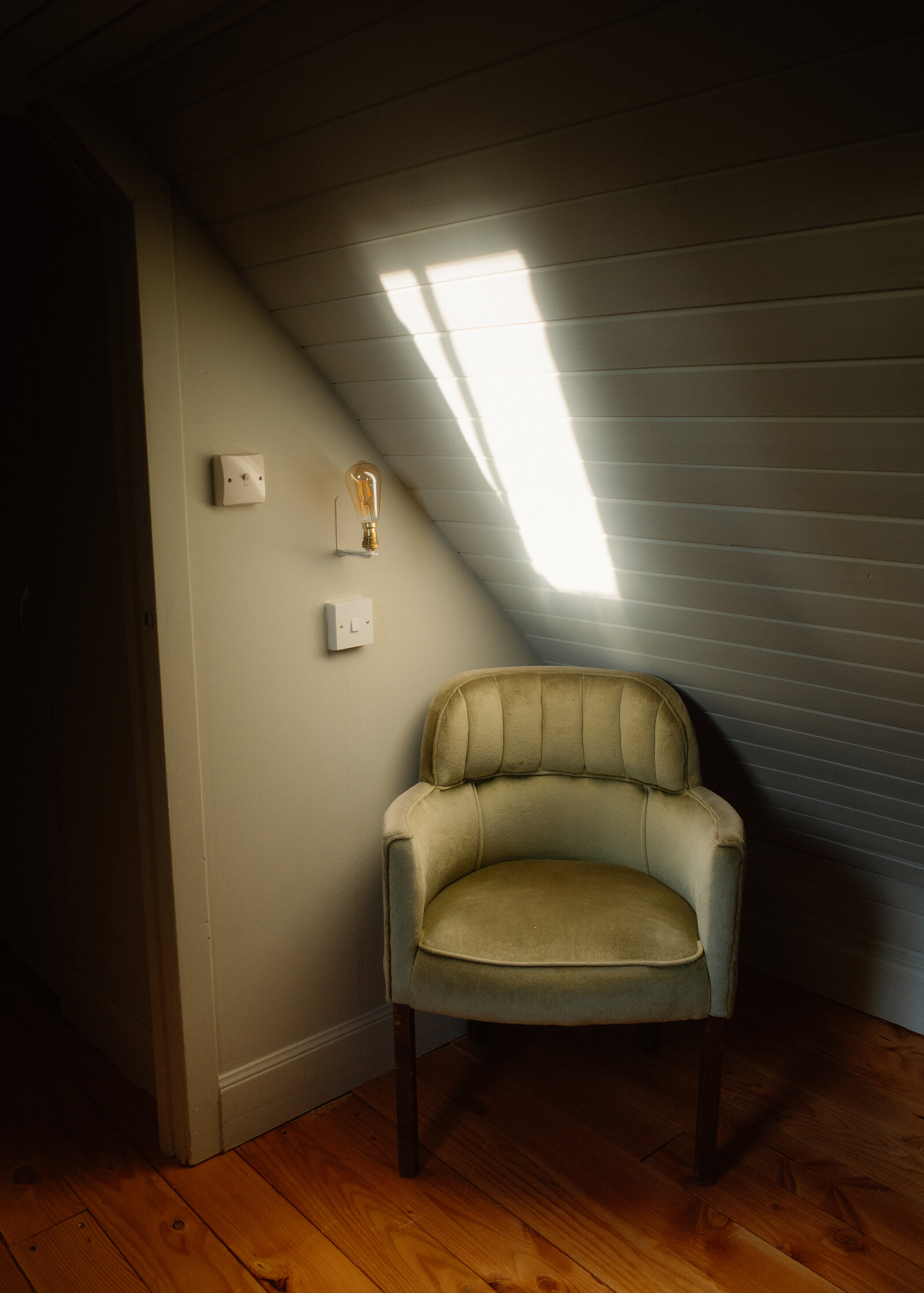 A green velvet armchair in an attic room under a skylight in the sloping ceiling.