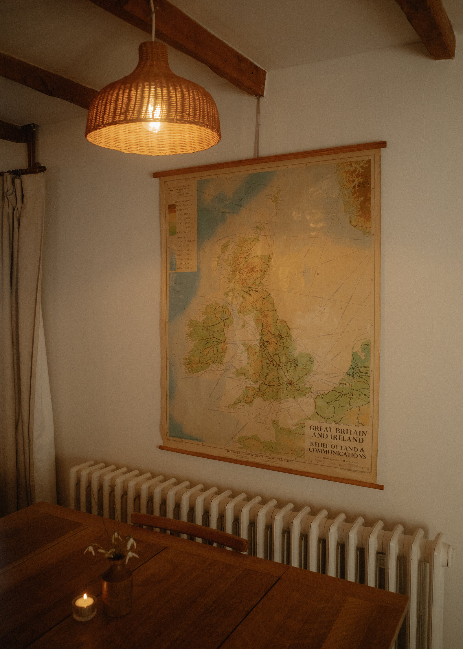 West Dell's dining room, an old map of Britain on the wall above the radiator and a wicker lampshade over the table.