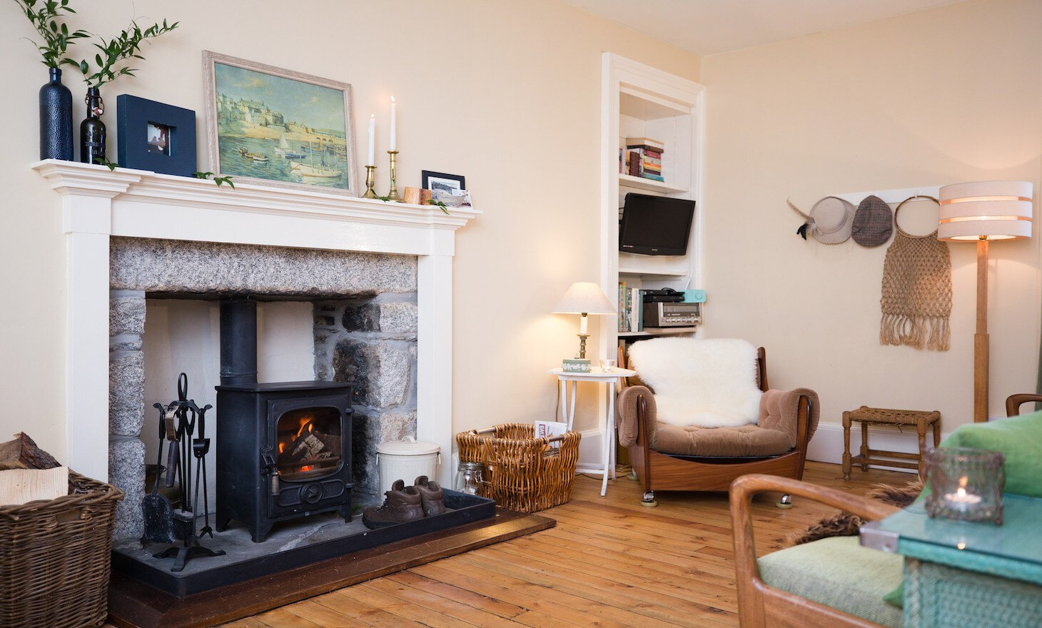 The sitting room, a stove lit in a granite surround with a white mantelpiece, an armchair and a sheepskin on the pitch-pine floor.
