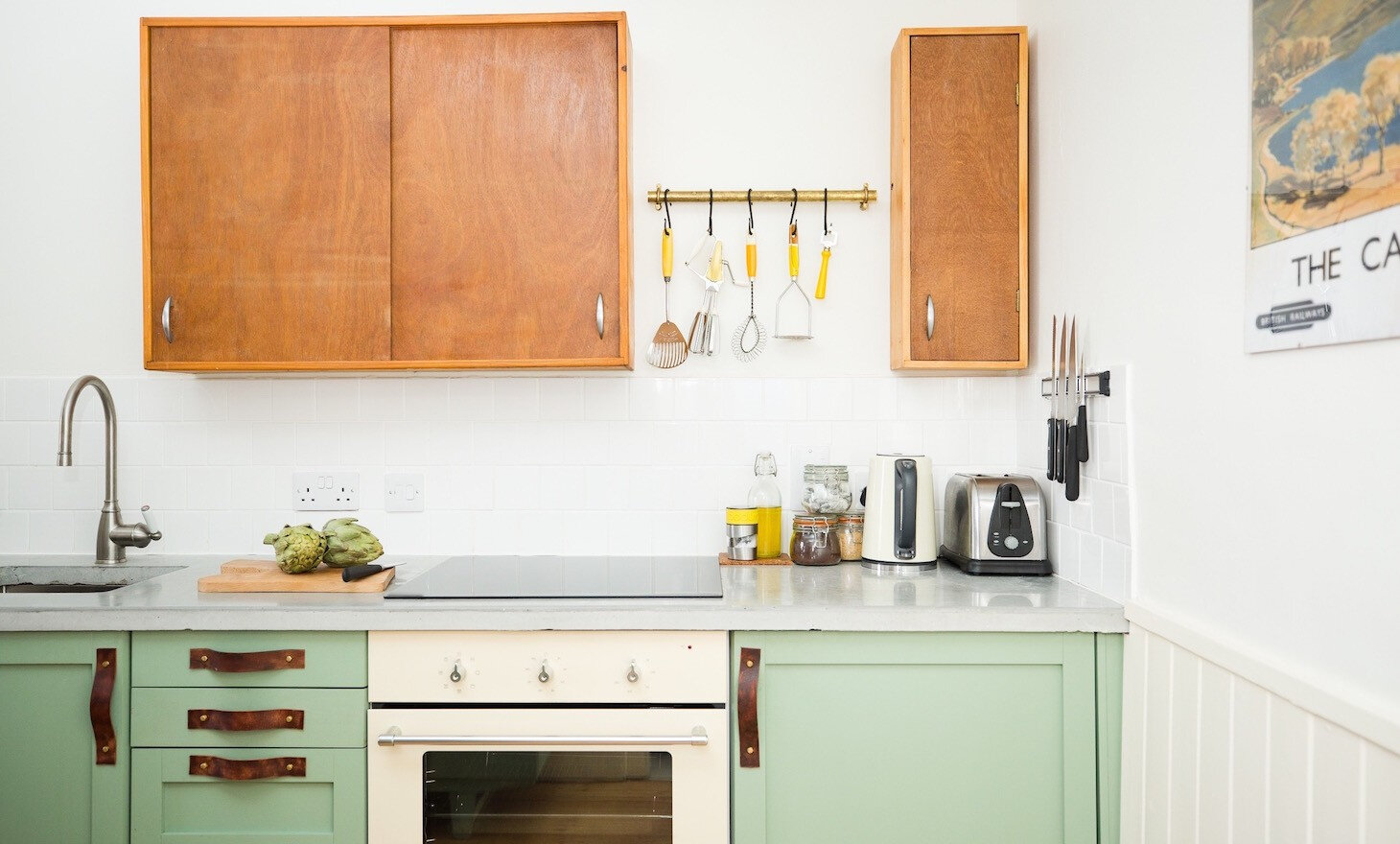 The vintage-style kitchen with sage-green units, wooden cupboards and a row of utensils on a rail.