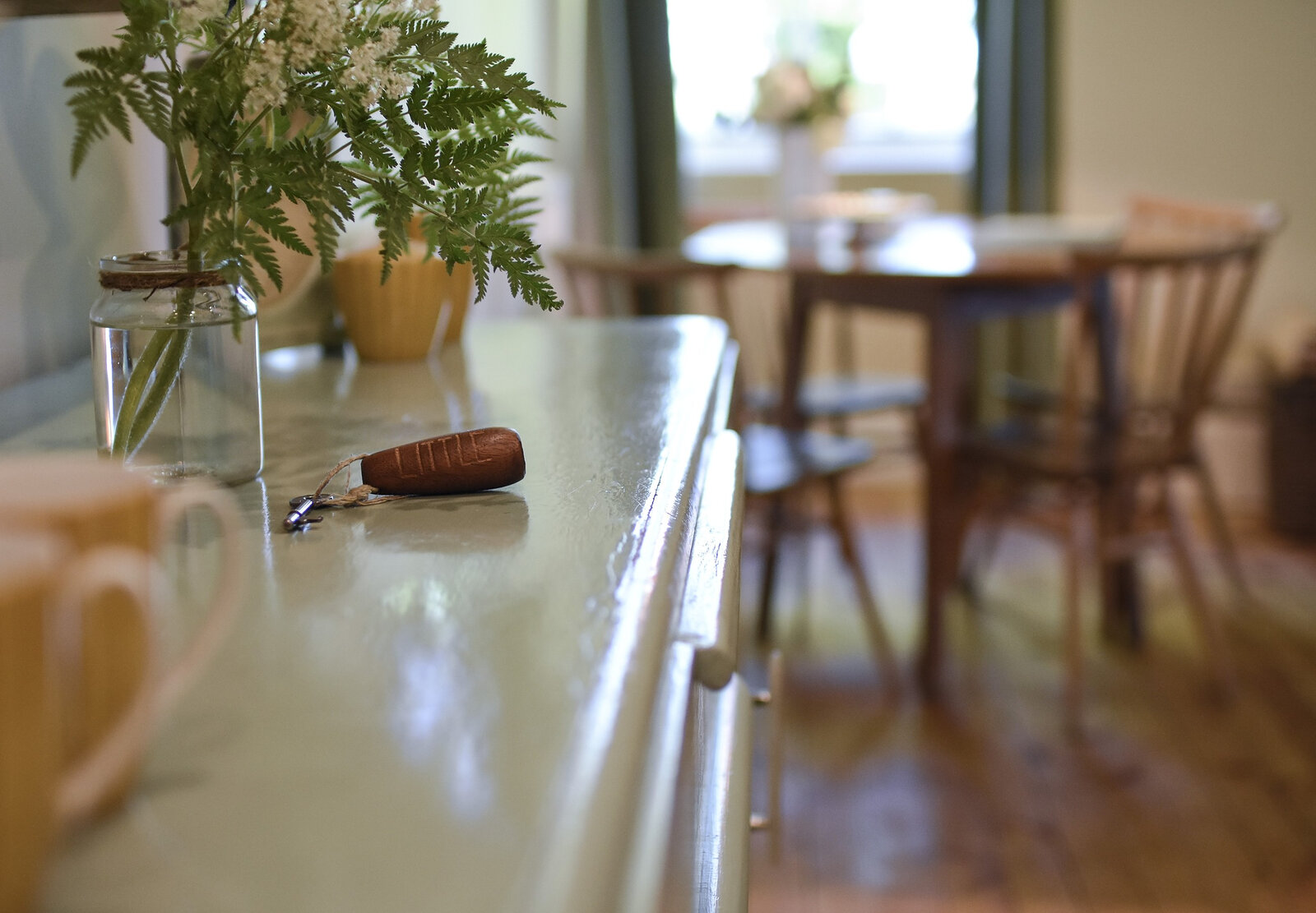 A key on the table by a jar of ferns, the dining room soft behind it.