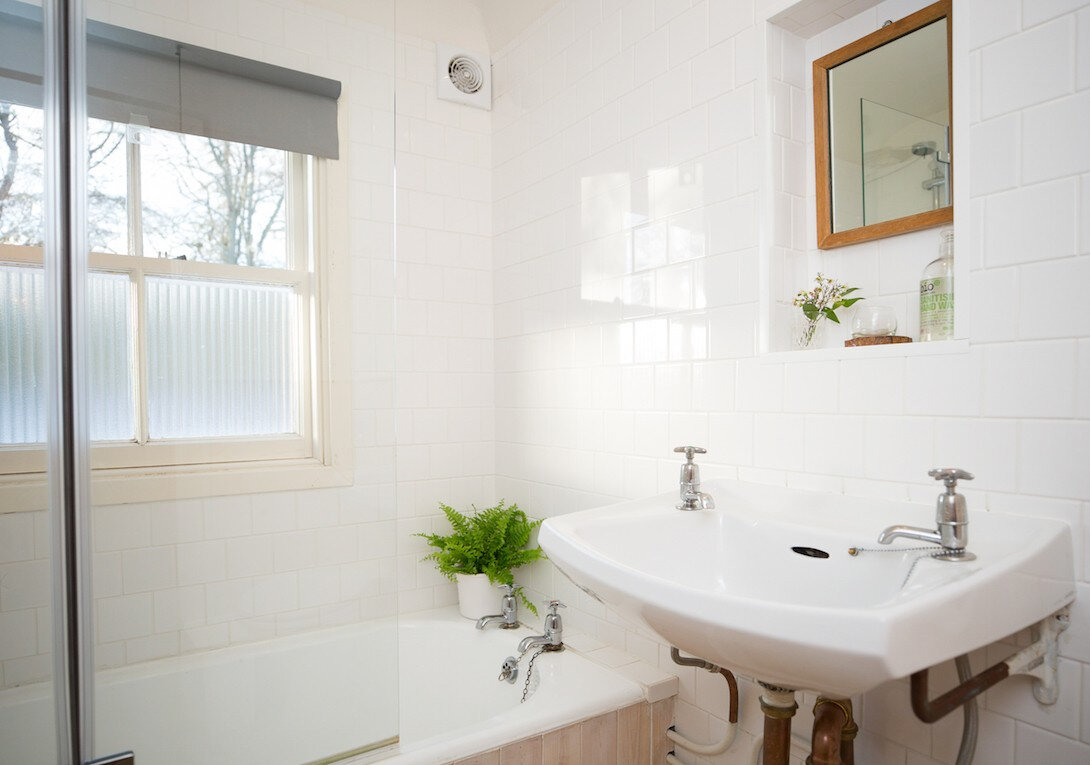 A white-tiled bathroom with a bath, an old-fashioned basin and a sash window.