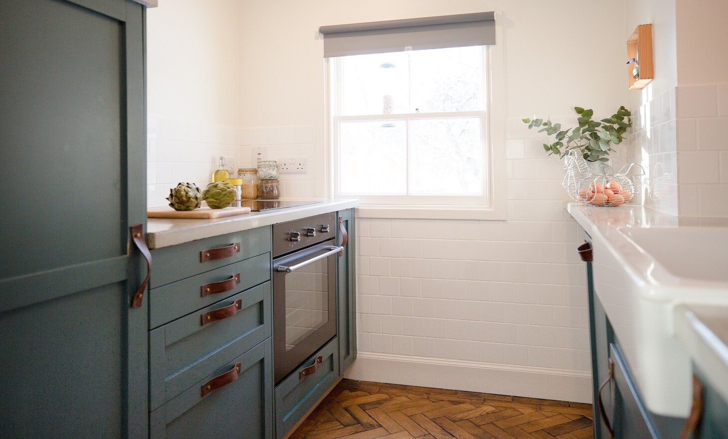 The kitchen with teal units and leather handles, a white butler's sink and a herringbone floor.