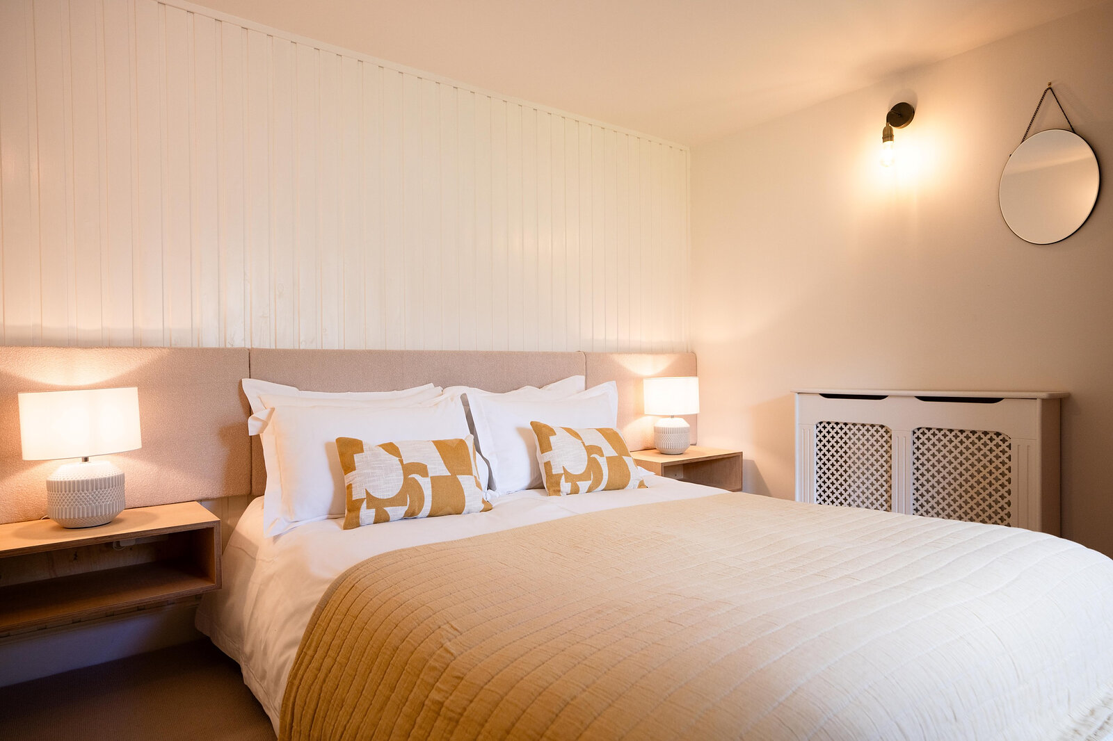 The ground-floor double bedroom, with white panelling, an ochre throw and lamps either side of the bed.
