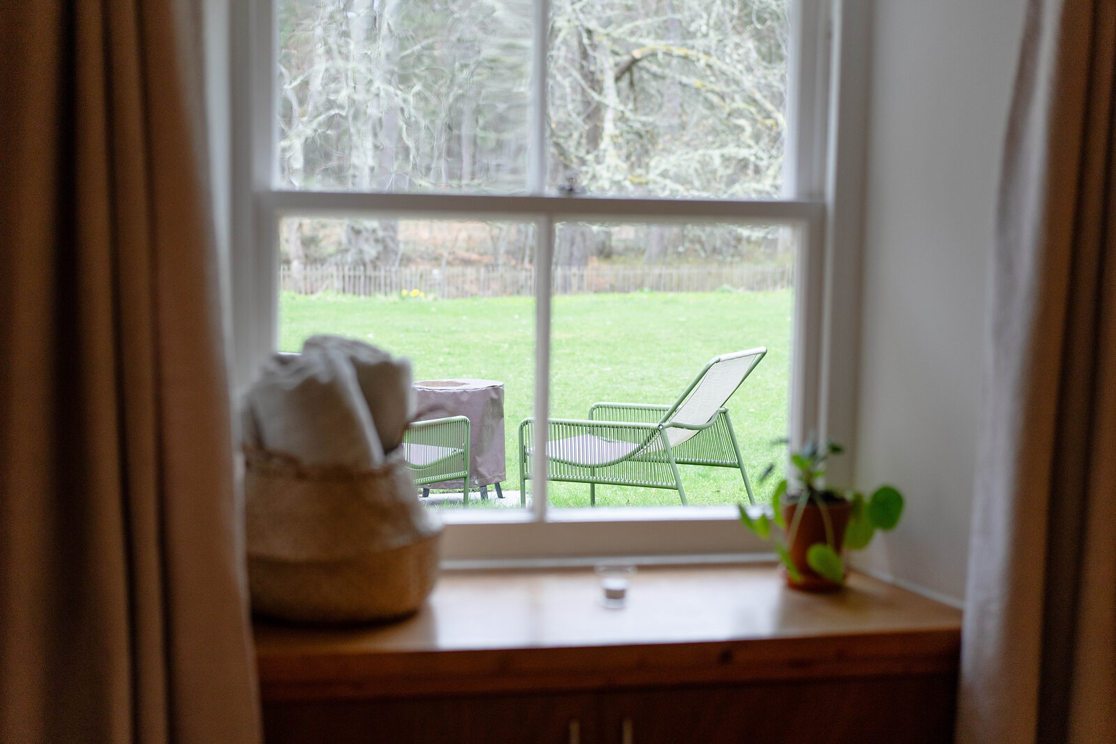 A window looking out onto the lawn, the garden chairs and the woods beyond.