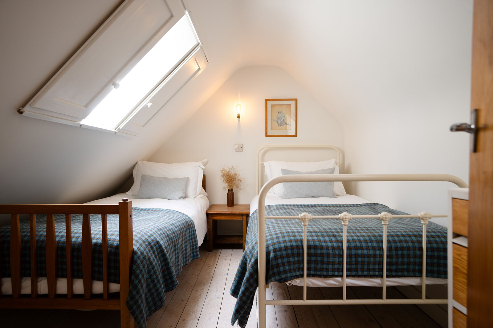 A twin room in the eaves with a skylight, tartan blankets and an iron bedstead.