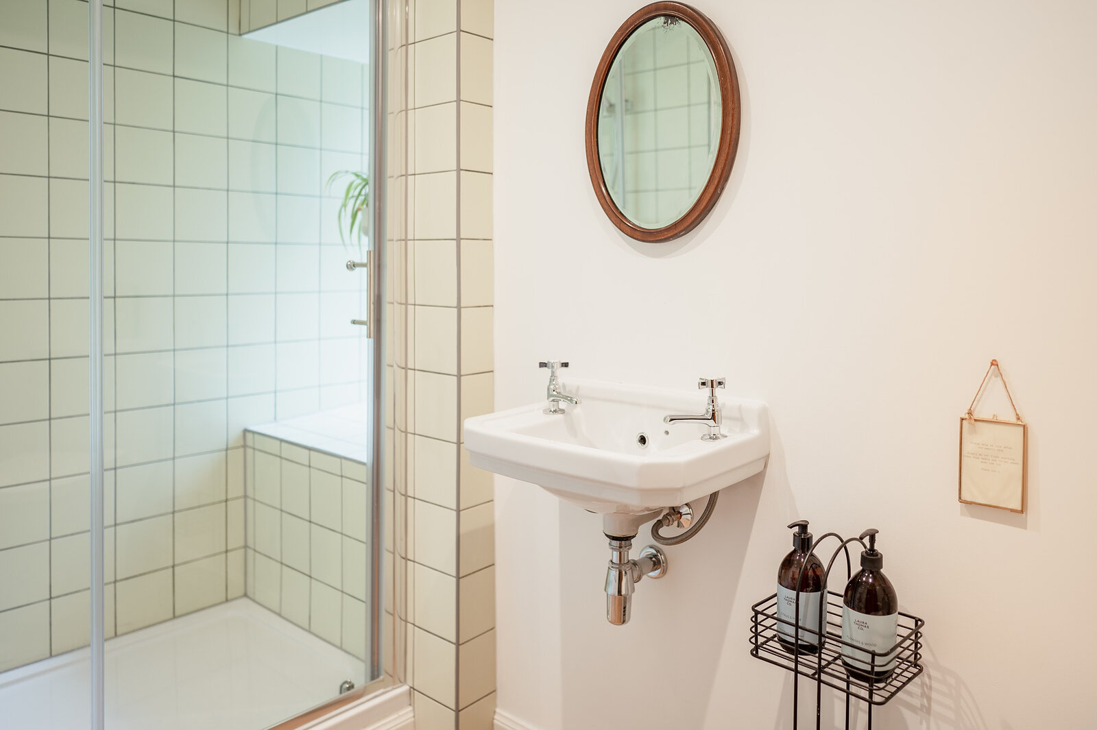 The shower room, with a glass shower, a small white basin and a round mirror.
