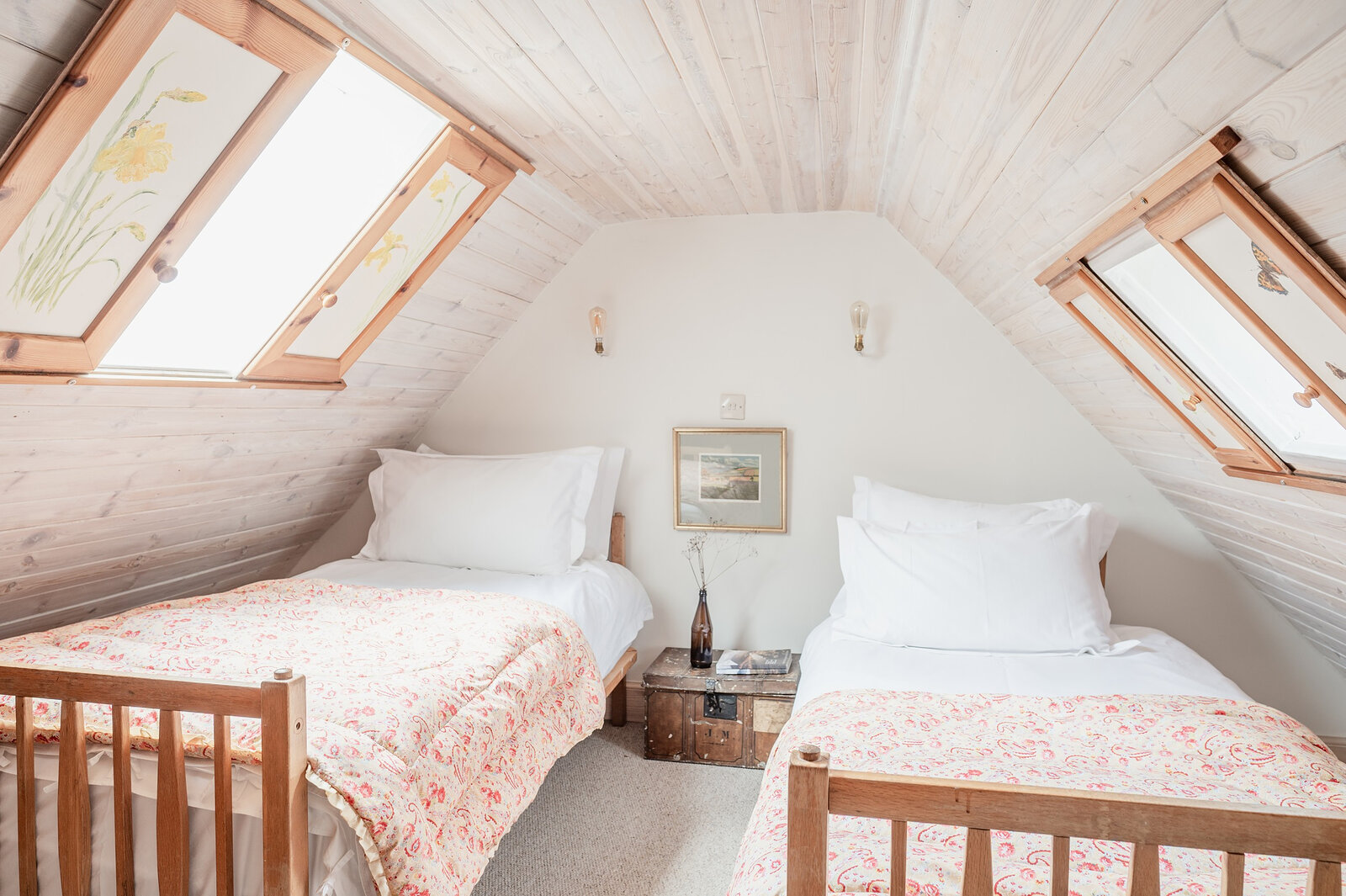 A twin room in the eaves, lit by two skylights, with floral covers on the beds.