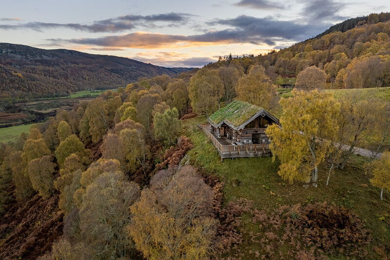 From above, Aquila's turf-roofed log cabin and wrap-around deck on the edge of the ridge, the glen stretching away in autumn colour.