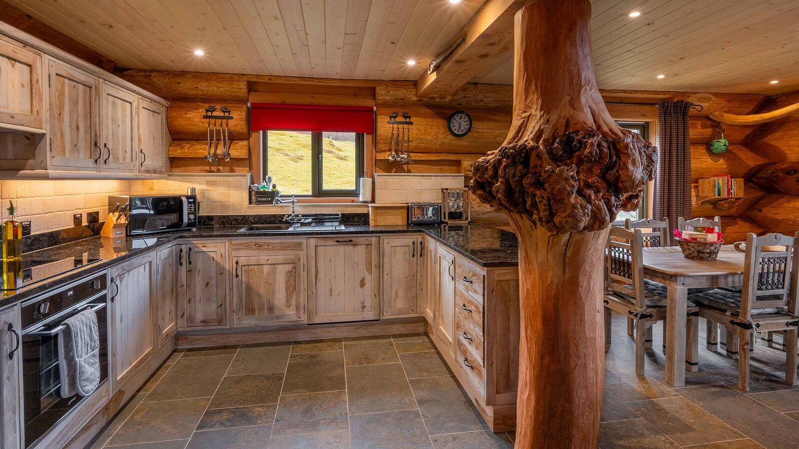 Aquila's kitchen of pale wood cupboards and dark worktops, a carved burr-wood post and the dining table beside it.