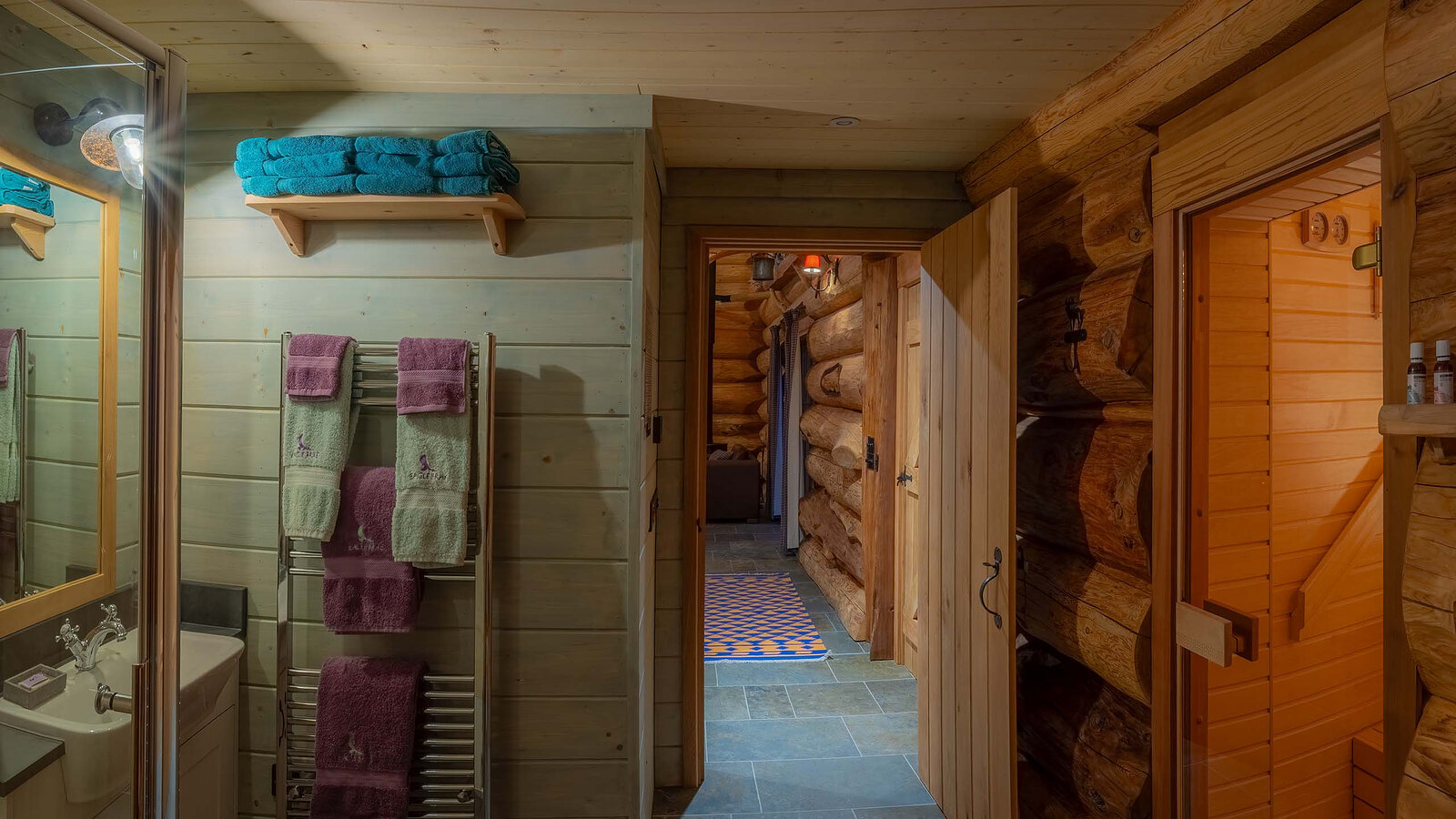 Aquila's bathroom with towels on a heated rail, the pine sauna door open beside it and the log hall beyond.