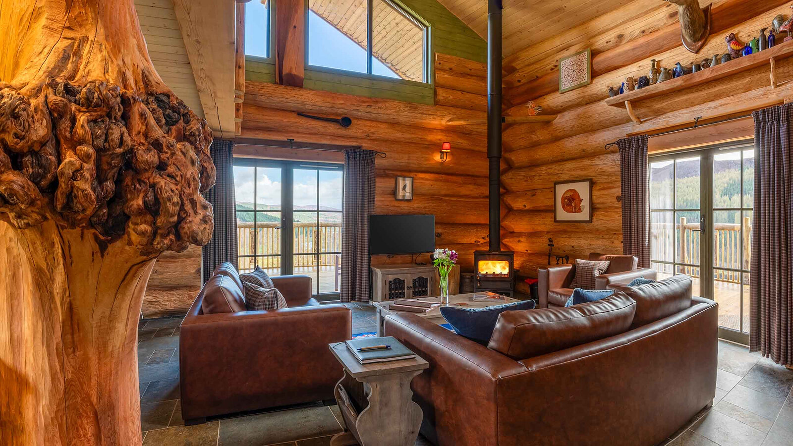 Aquila's living room under the high log gable: leather sofas round the wood stove, glass doors to the deck on either side.
