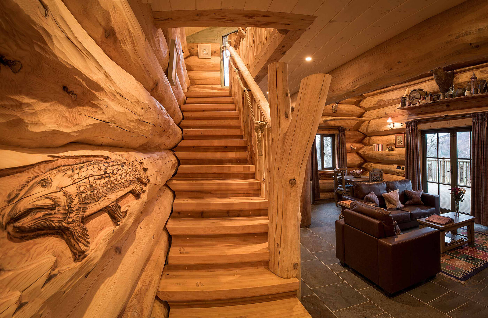 A salmon carved into the log wall beside Ardea's stair, the living room and its sofas beyond.