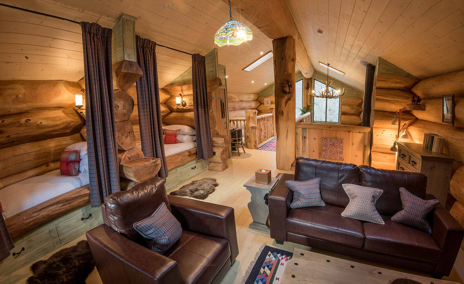 Ardea's mezzanine sitting room, leather sofas under a stained-glass lamp and the curtained log beds behind.