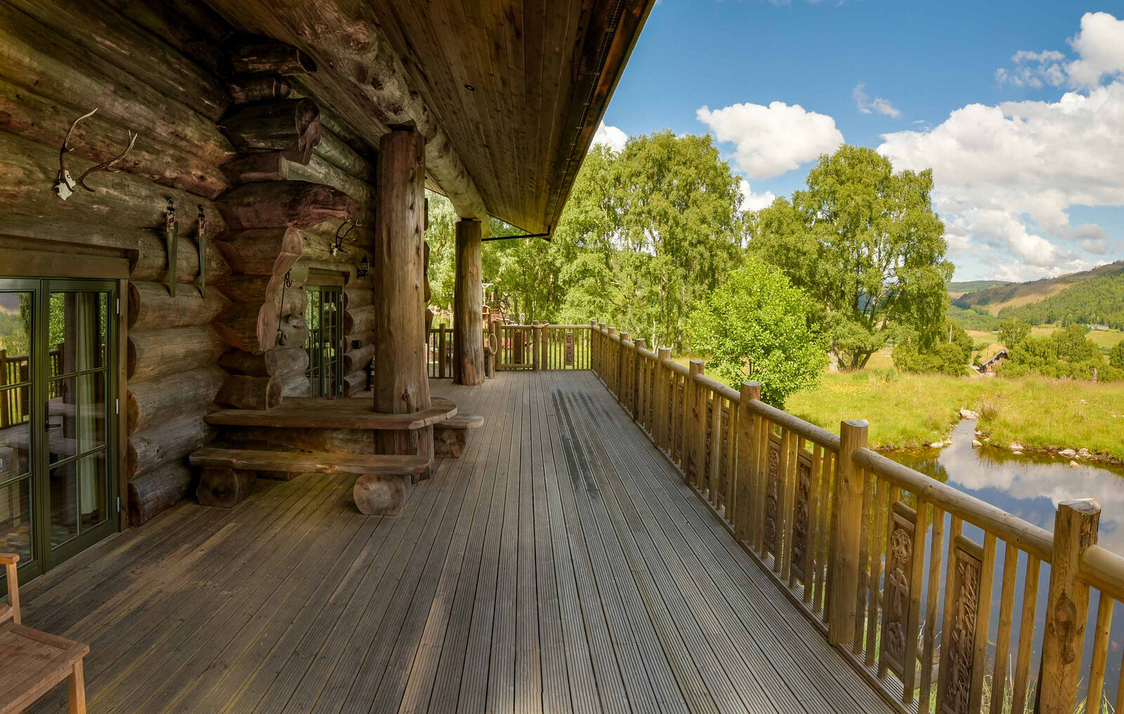 Ardea's long covered deck with carved railings above the pond, a log bench against the wall and the glen beyond.