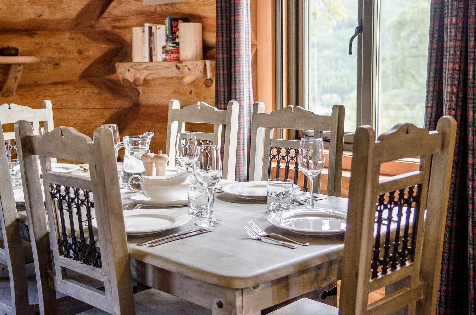 A table laid for a meal in Buteo, carved grey chairs and glasses by the tall window and its tartan curtains.