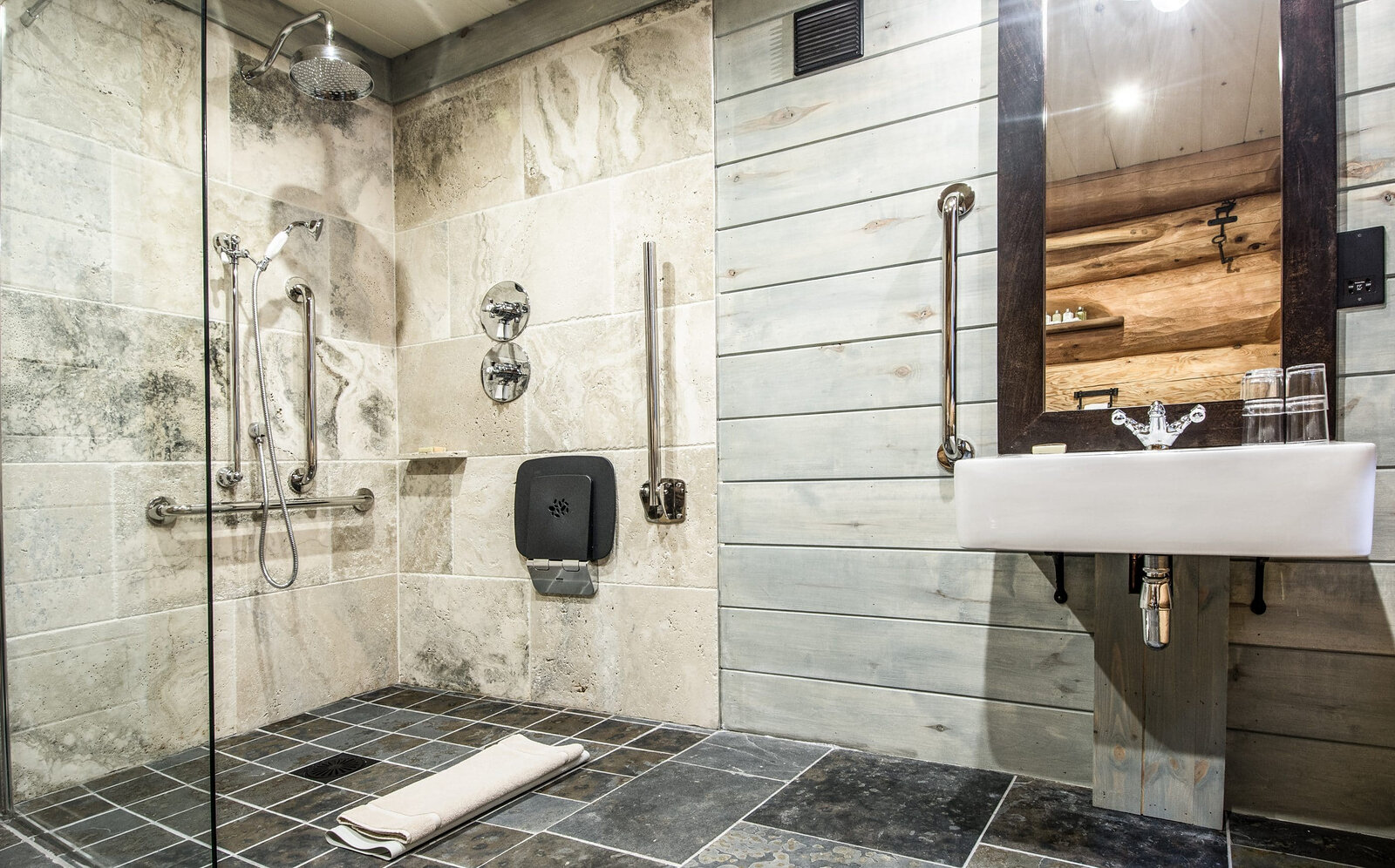 Buteo's step-in shower room with a rainfall shower, grab rails and a basin on grey stone and wood.