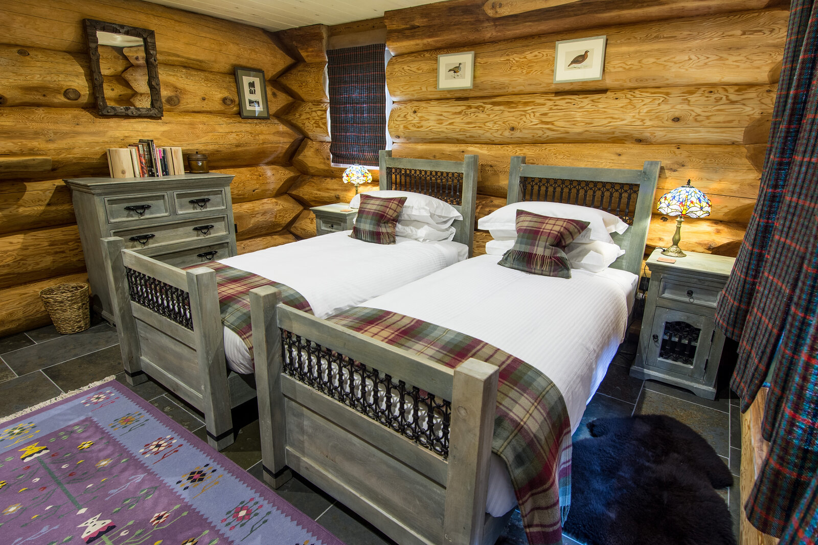 Buteo's twin room: two carved beds with tartan throws on a Himalayan rug, bird prints on the log wall.