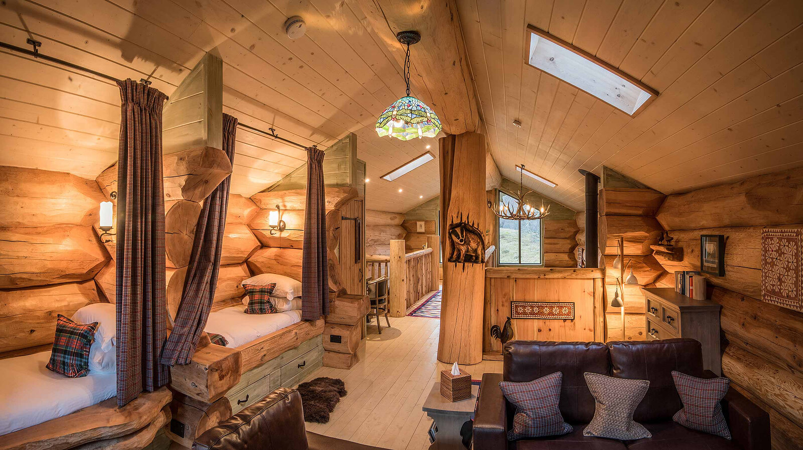 Certhia's mezzanine: curtained log beds and a leather sofa under skylights and a stained-glass lamp.