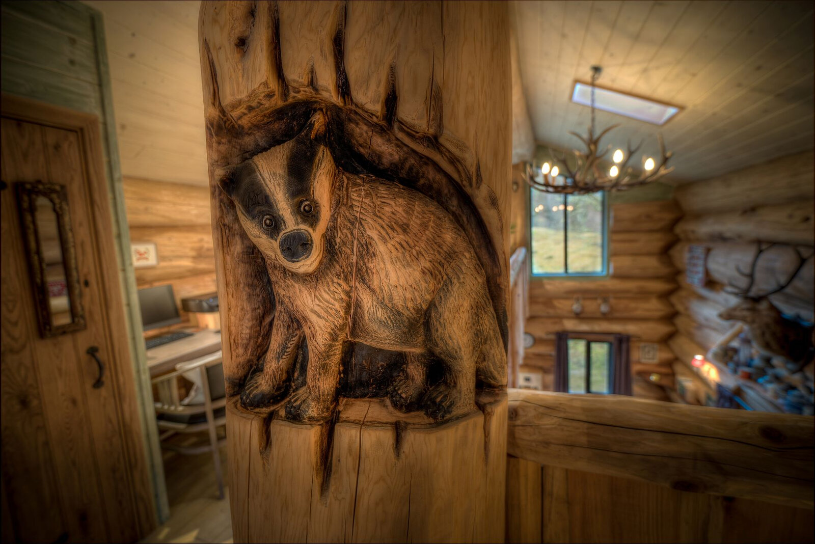 A badger carved into a log post in Certhia, the office nook and an antler chandelier beyond.