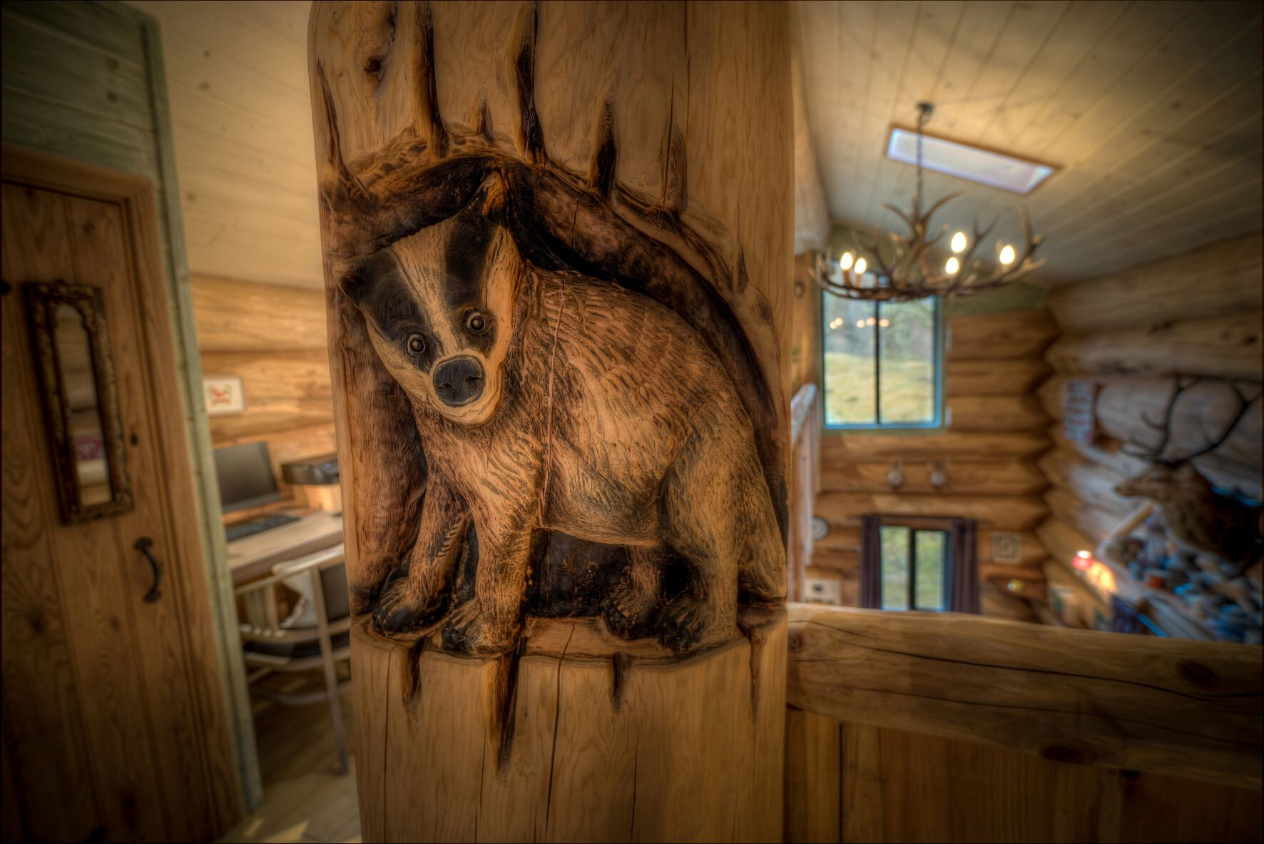 A badger carved into a log post in Certhia, the office nook and an antler chandelier beyond.