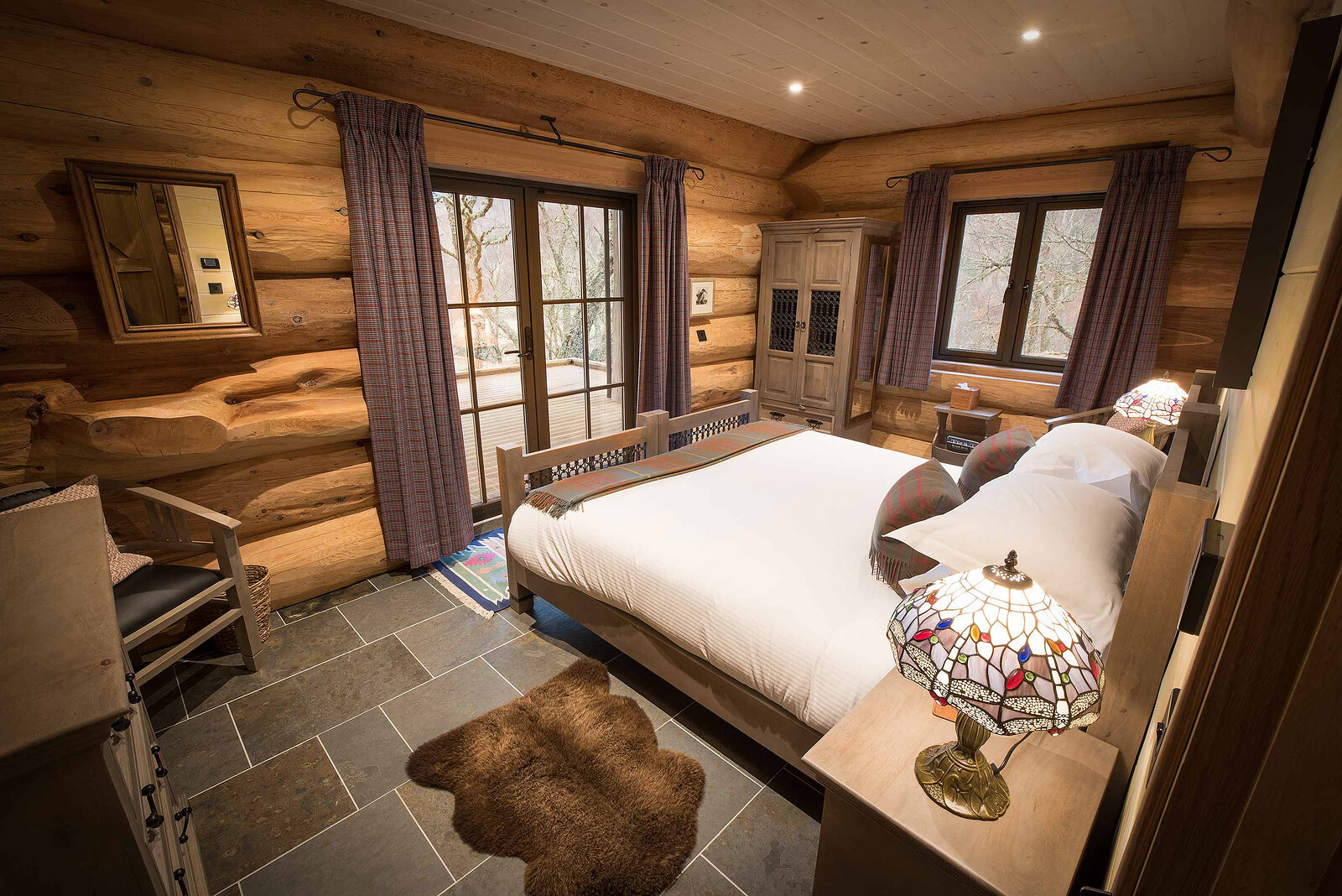 Certhia's bedroom on a slate floor: a carved bed, a dragonfly lamp and glass doors behind tartan curtains.