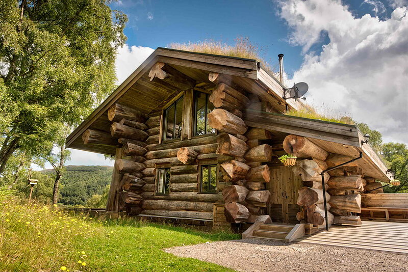 Certhia on its ridge: a two-storey log cabin of great notched logs under a turf roof, steps up to the door.
