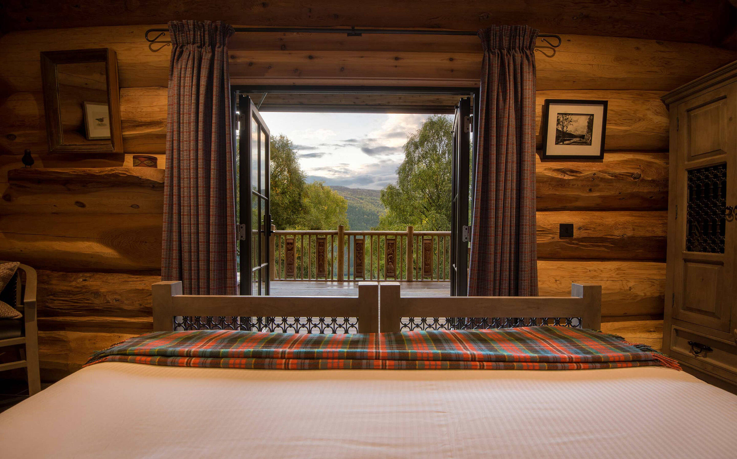 From Cinclus's bed through the open glass doors, the carved deck rail and the glen under a cloudy sky.