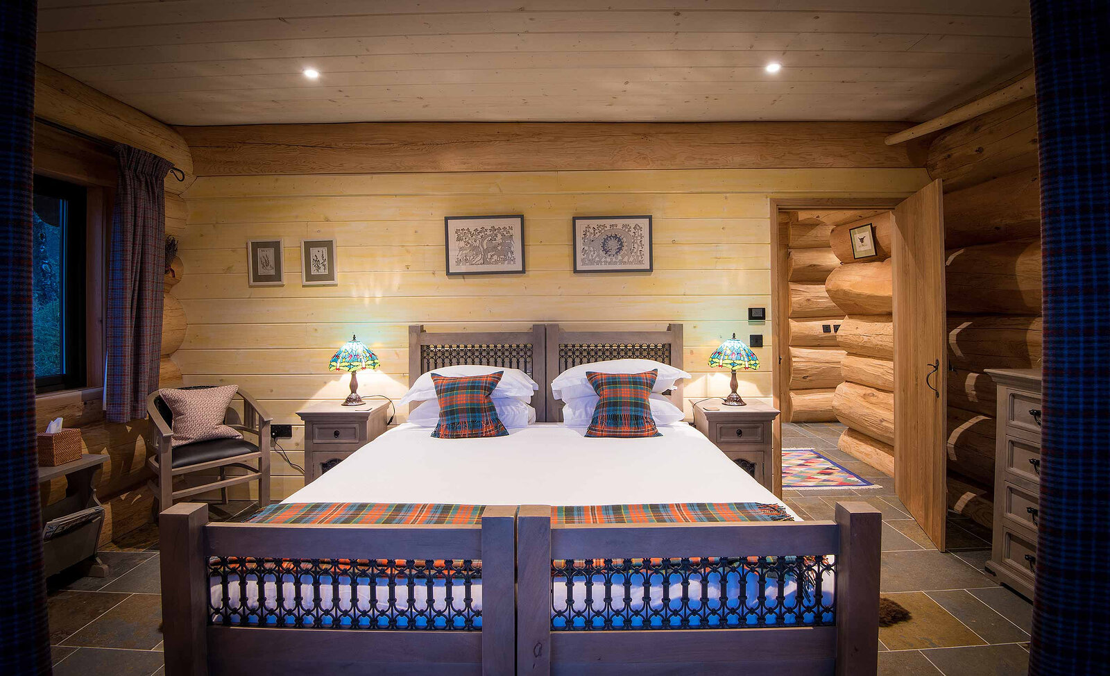 Cinclus's bedroom: a carved bed with tartan cushions between stained-glass lamps, Himalayan prints on the pale boards.