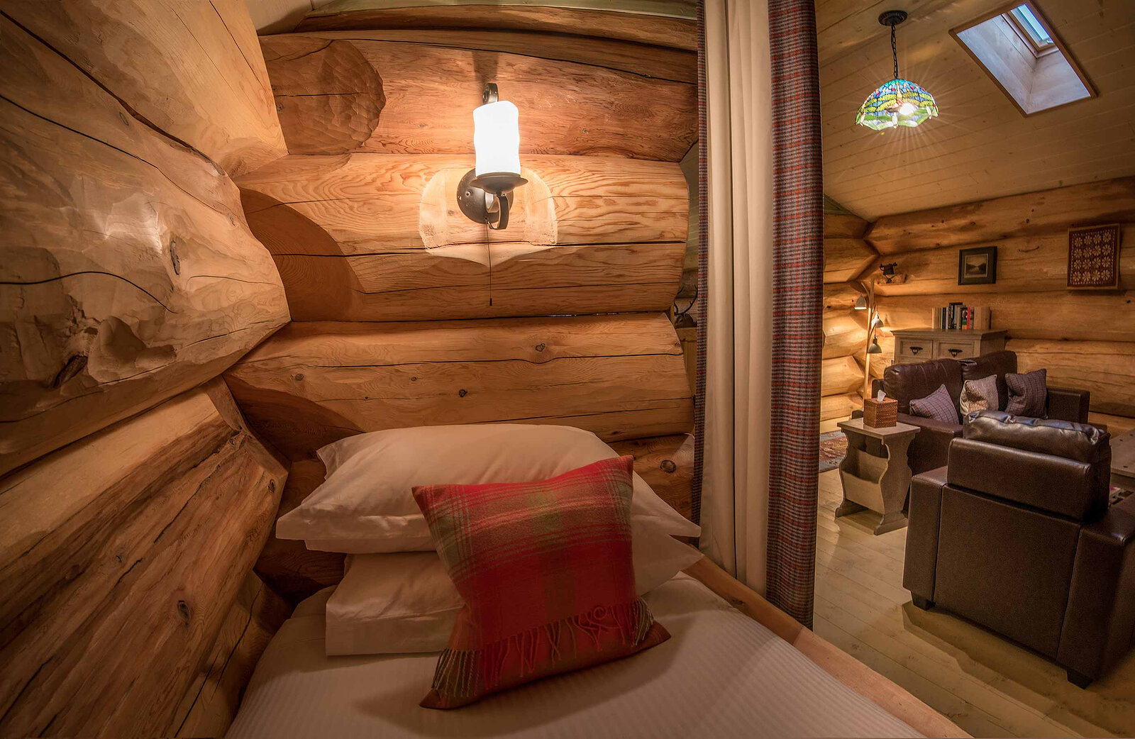 A curtained log bed in Cinclus's mezzanine with a red tartan cushion, the sitting room beyond.